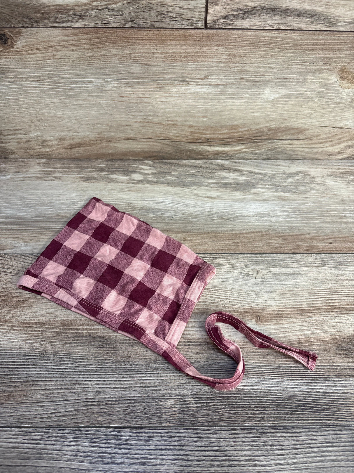 Flat lay of red and pink gingham baby bonnet size 12–18 months showing check pattern and chin ties on light wood background