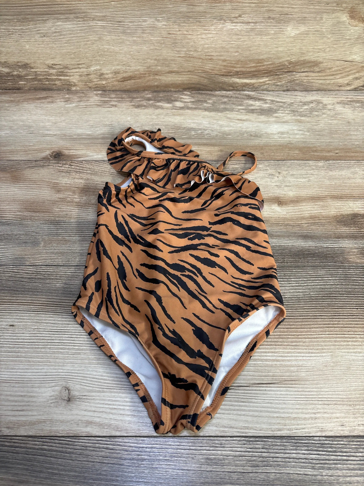 Front view of Carter’s one-piece swimsuit in size 3T with brown tiger-stripe pattern and ruffled straps on wood background