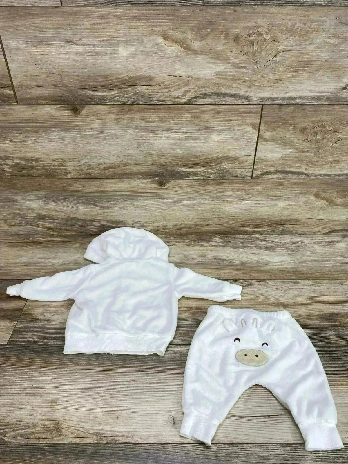 Flat lay of white terry cloth hoodie (back) and matching pants showing embroidered animal face on wood floor background