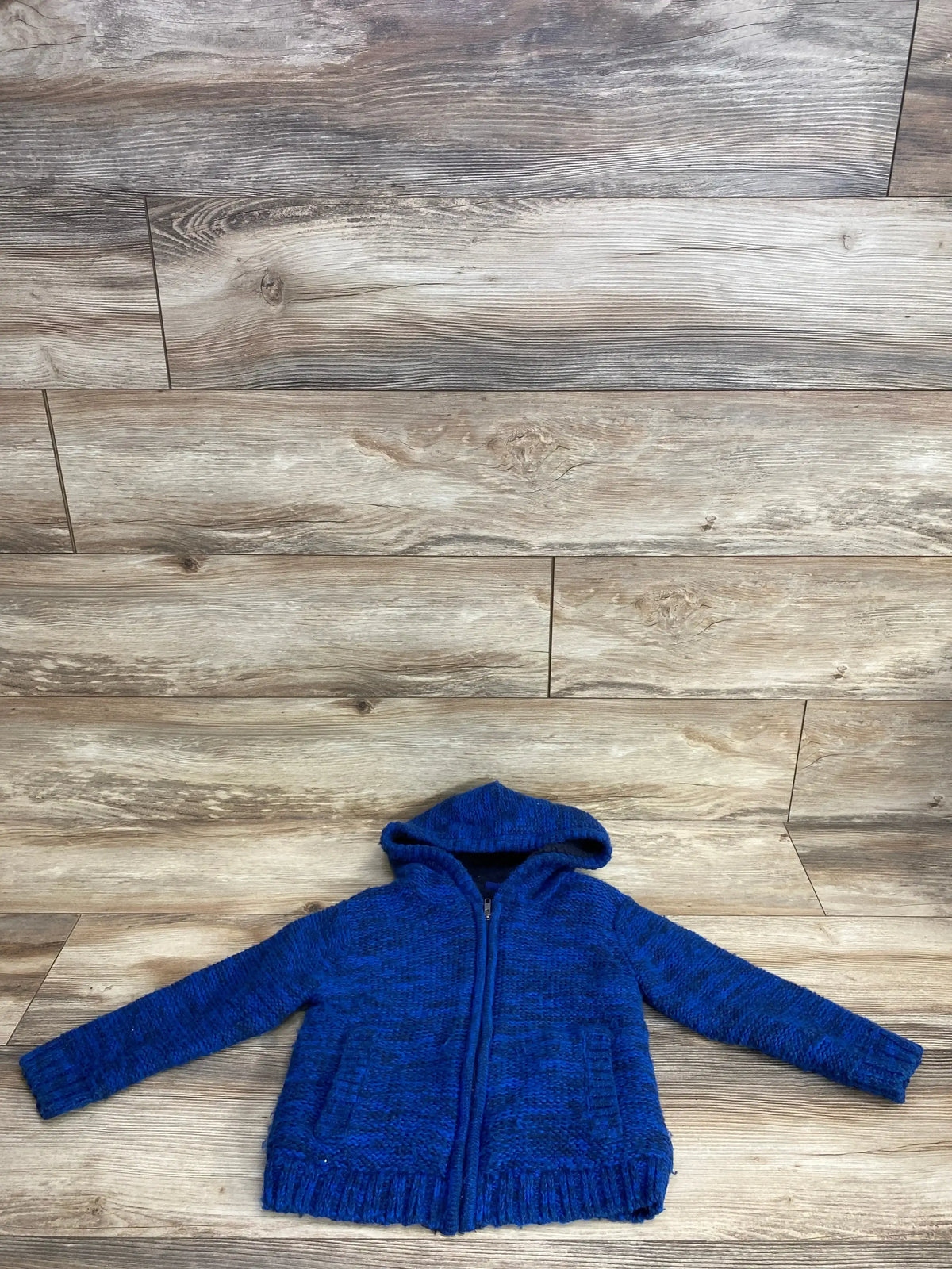 Blue knit hooded zip-up sweater for kids displayed on a wooden floor background