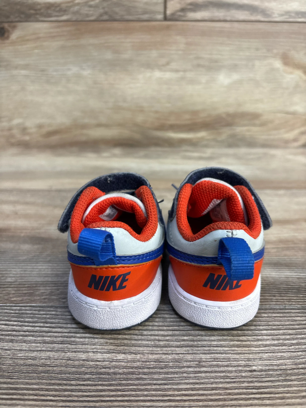 Back view of Nike Court Borough Low Recraft sneakers showing orange heel, navy pull tab and NIKE logo on wood floor