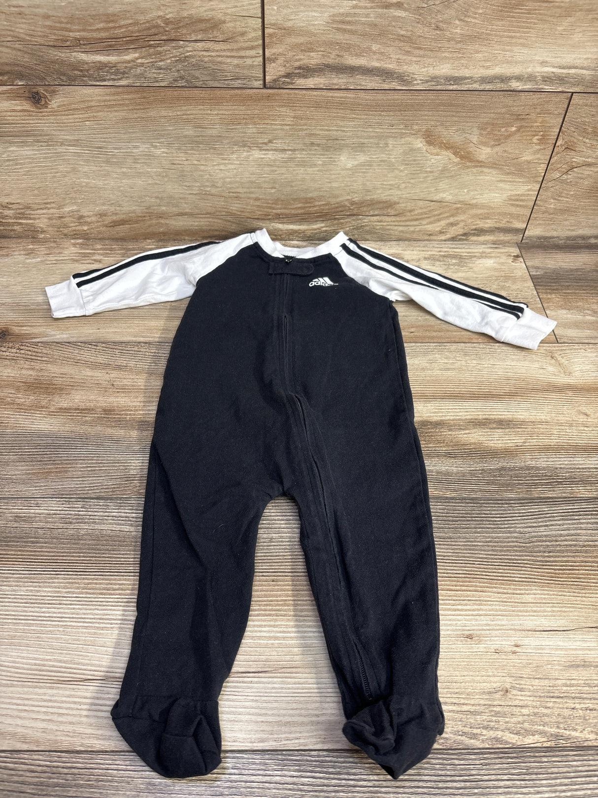 Black and white Adidas infant onesie with stripes on sleeves laid on wooden floor