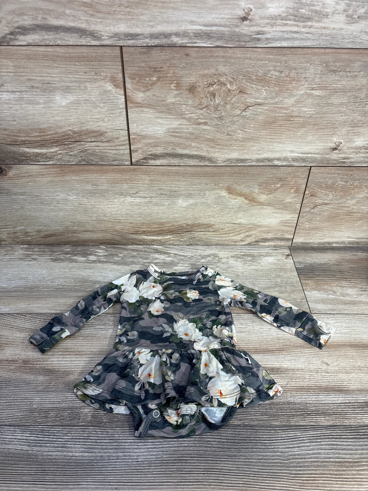 Flat lay of Gigi & Max bamboo floral camo tutu bodysuit showcasing the tutu detail and long sleeves on a wood floor