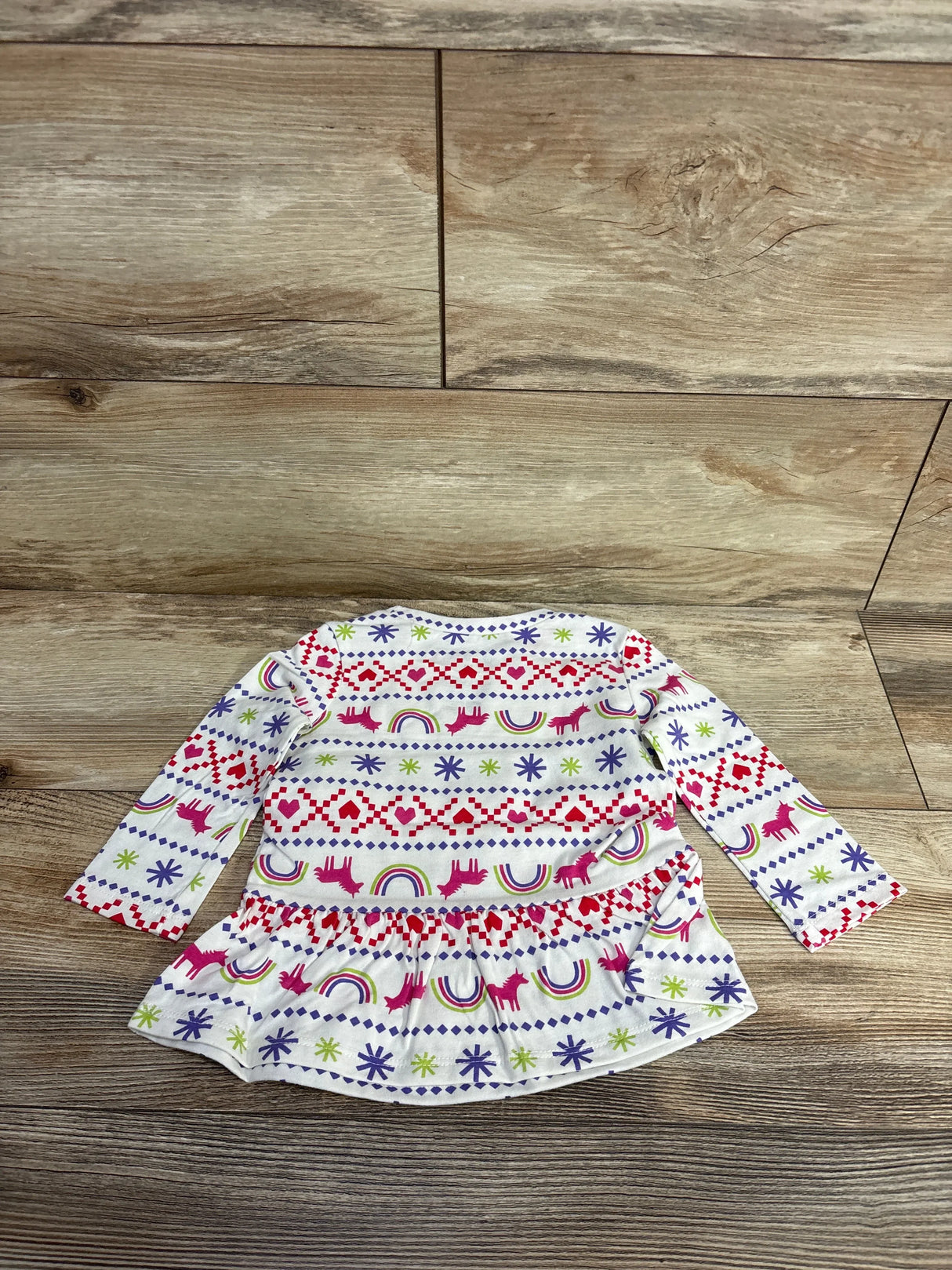 White long-sleeve toddler dress with pink unicorns, rainbows, hearts, and stars on wood floor