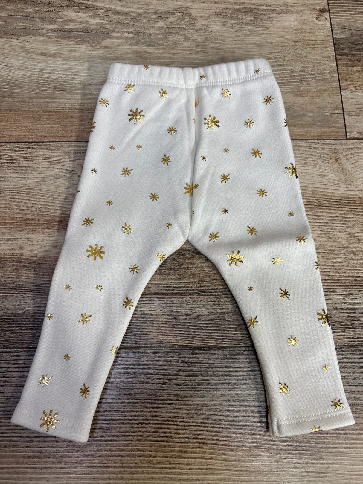 White toddler leggings with gold star and snowflake pattern on wooden floor