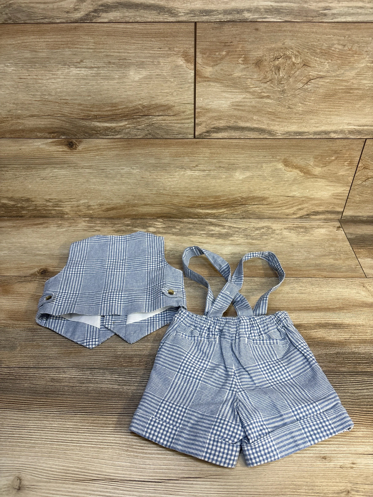 Blue and white gingham baby boy outfit with suspenders and matching top on wood floor