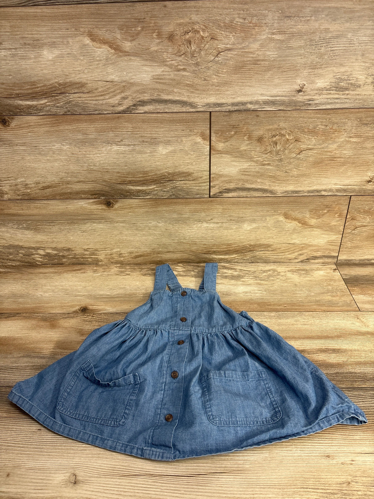 blue denim toddler dress with front buttons and two pockets on wooden background