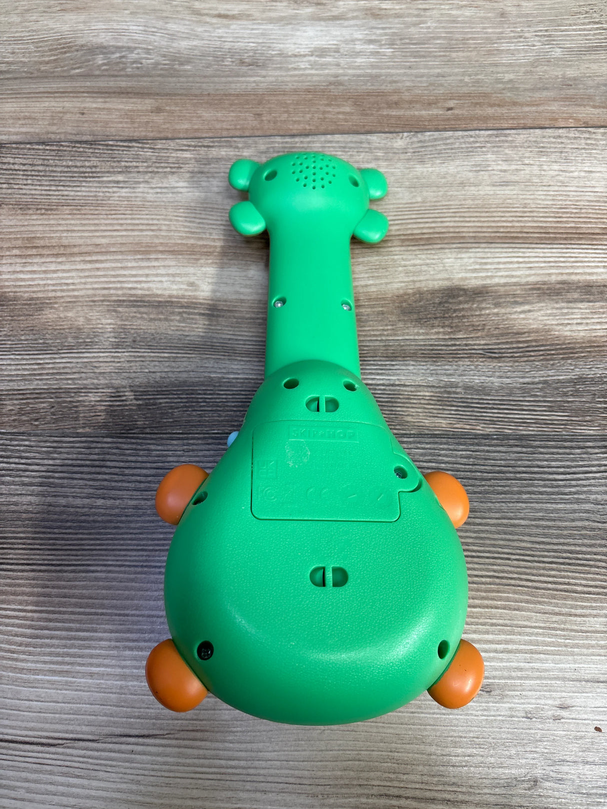 Green Skip Hop giraffe-shaped baby toy on wooden surface with orange feet details