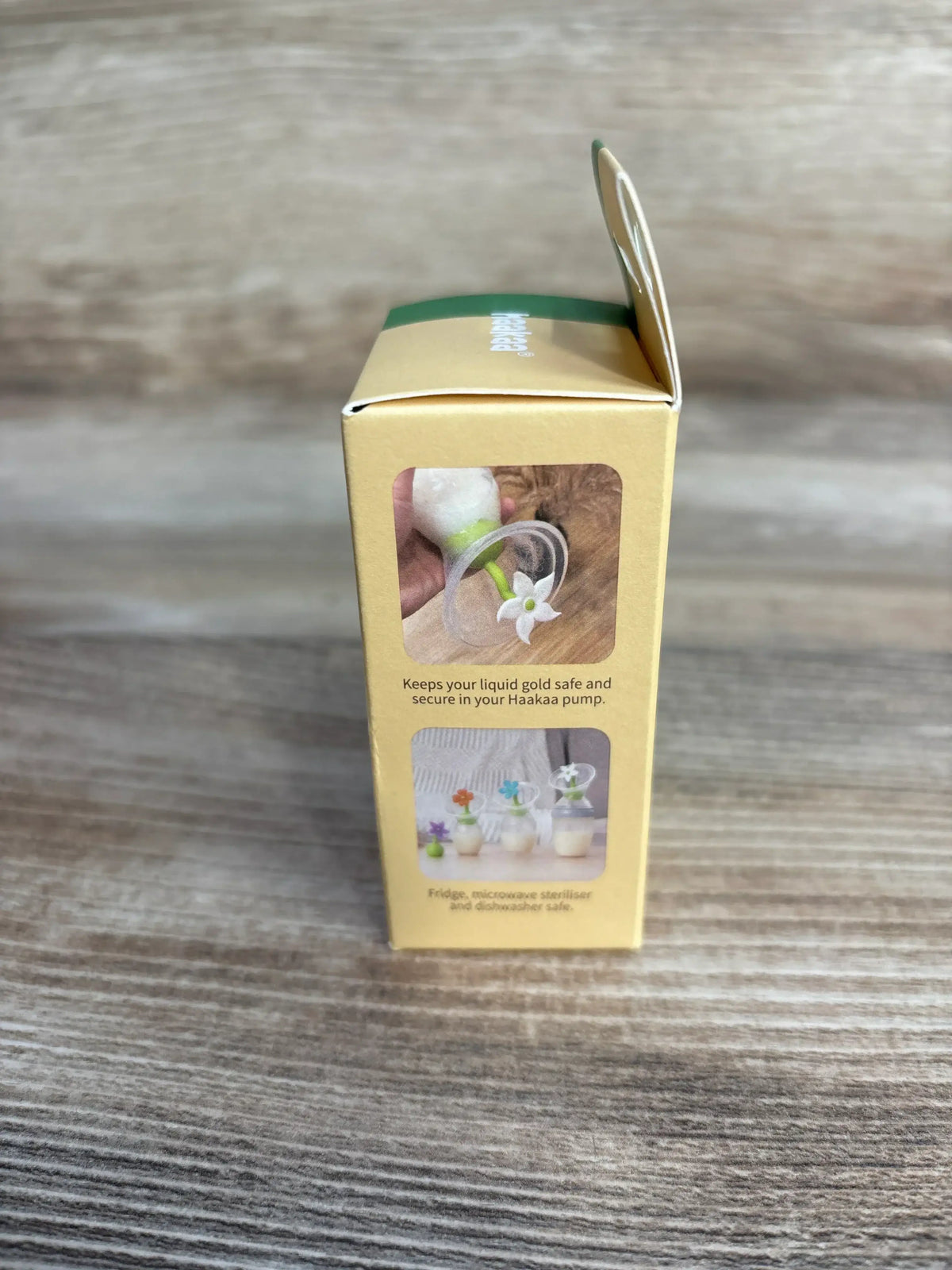 Front of Haakaa flower stopper box showing product photo and the text Keeps your liquid gold safe and secure in your Haakaa pump on a wood surface