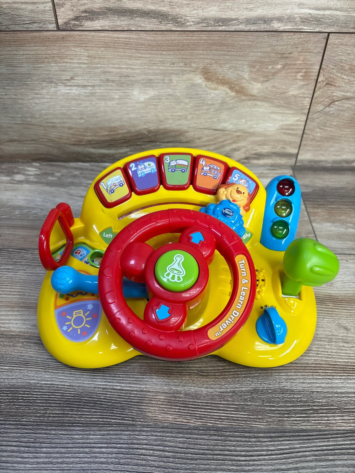 Front view of Vtech Turn & Learn Driver with steering wheel, activity buttons, lights, gear shift, and signal lever