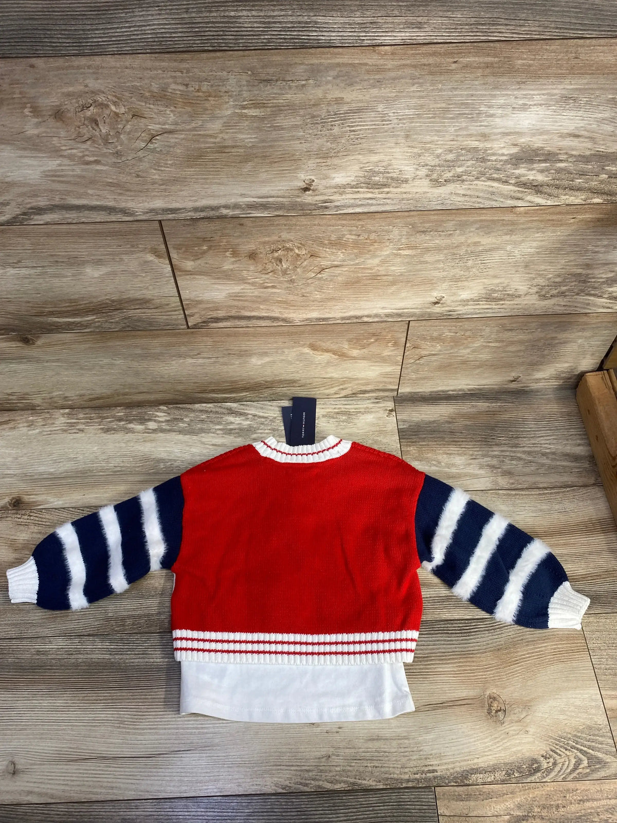 Red kids sweater with navy and white striped sleeves on wood floor