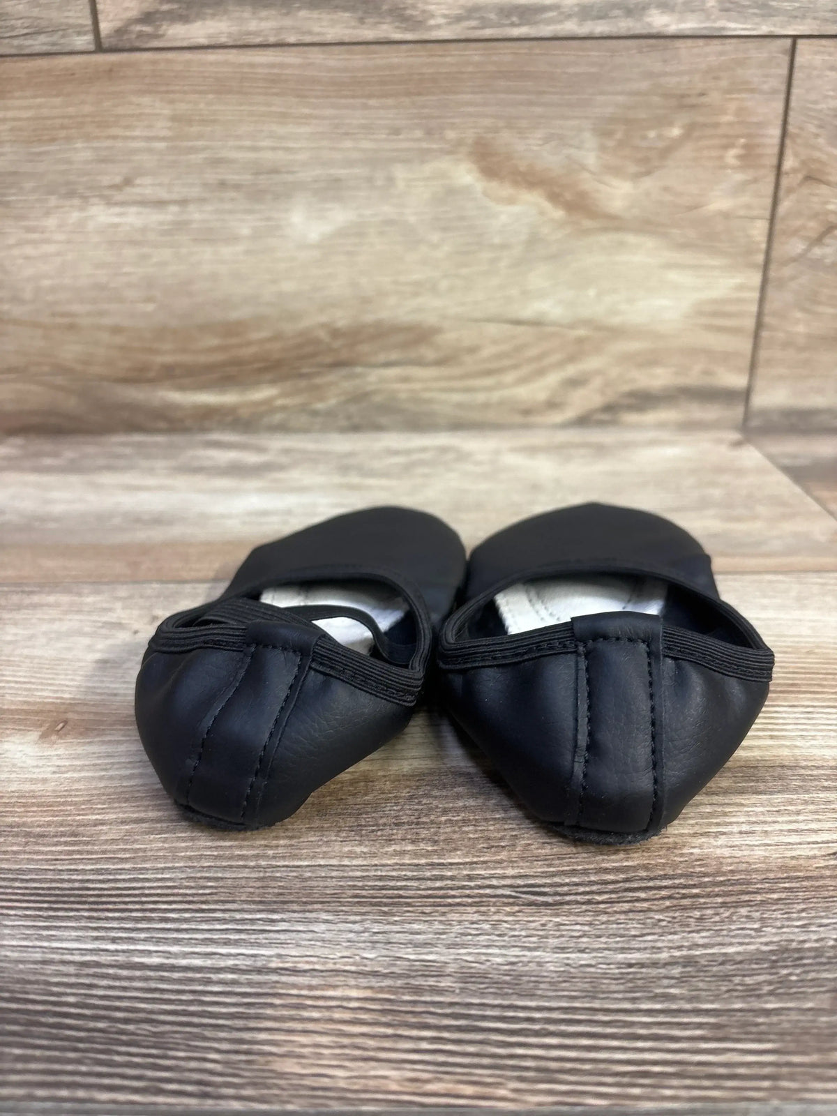 Front view of black ballet shoes (child size 6/7C) showing elasticized toe and stitched heel on wood floor background