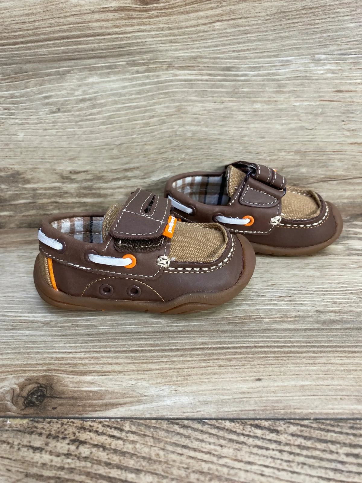 Side view of brown Pediped Naples loafer showing velcro strap, white lace trim, orange accents and plaid lining on wood