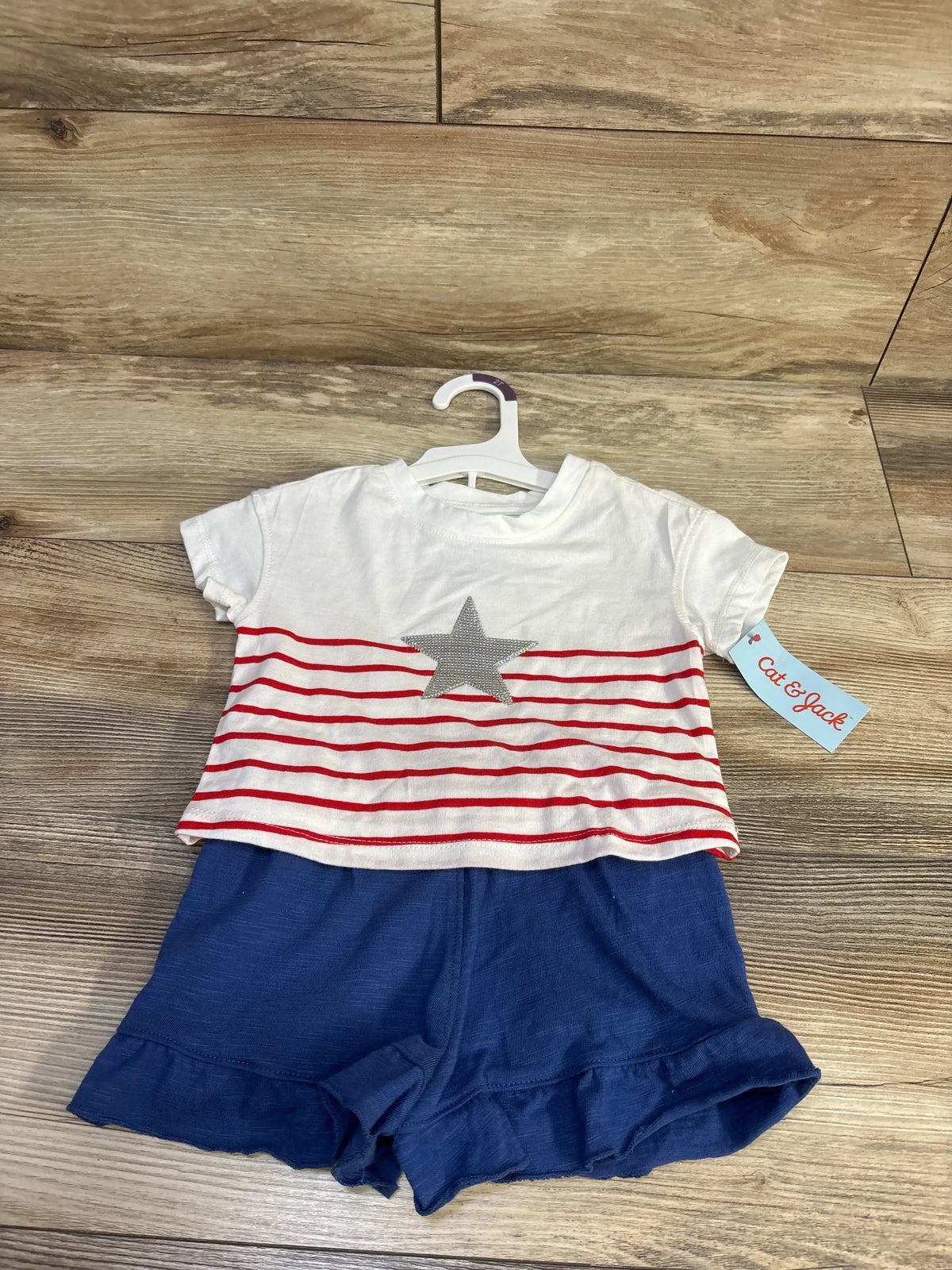 Front view of toddler 2-piece Fourth of July outfit: white tee with red stripes and silver star and blue ruffle shorts