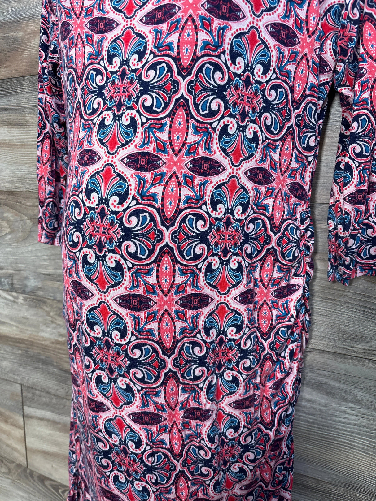 Close-up front of Jessica Simpson pink maternity dress size XL showing ruched side seam and navy and pink geometric floral print on wood background