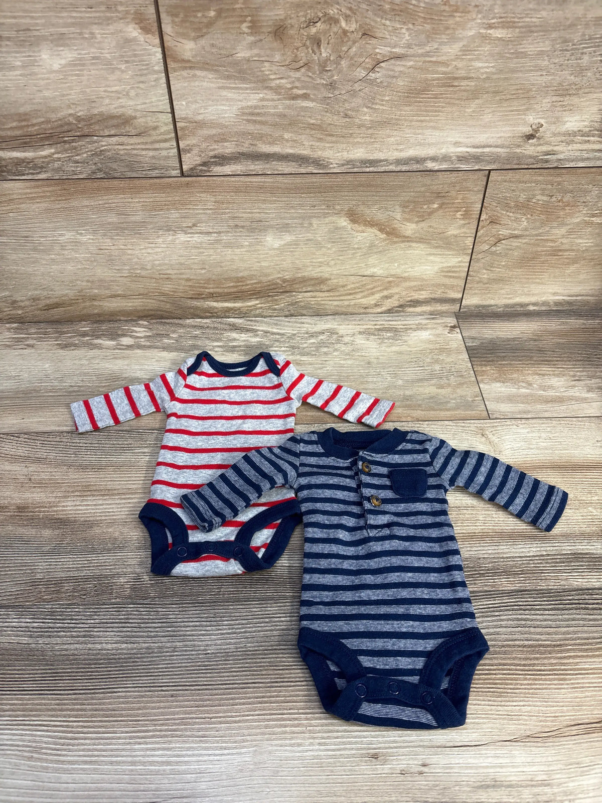 Overhead view of Child Of Mine two pack preemie bodysuits showcasing striped long sleeves and snap closures on a wood floor