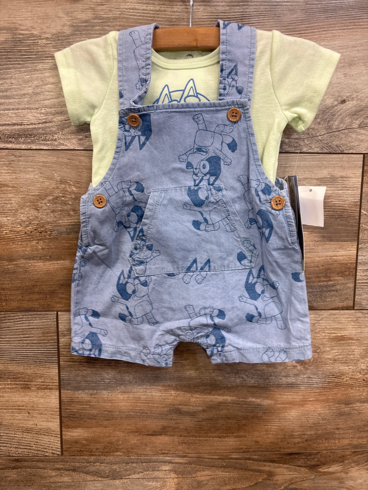Baby outfit with yellow t-shirt and blue cartoon print overalls on wooden background