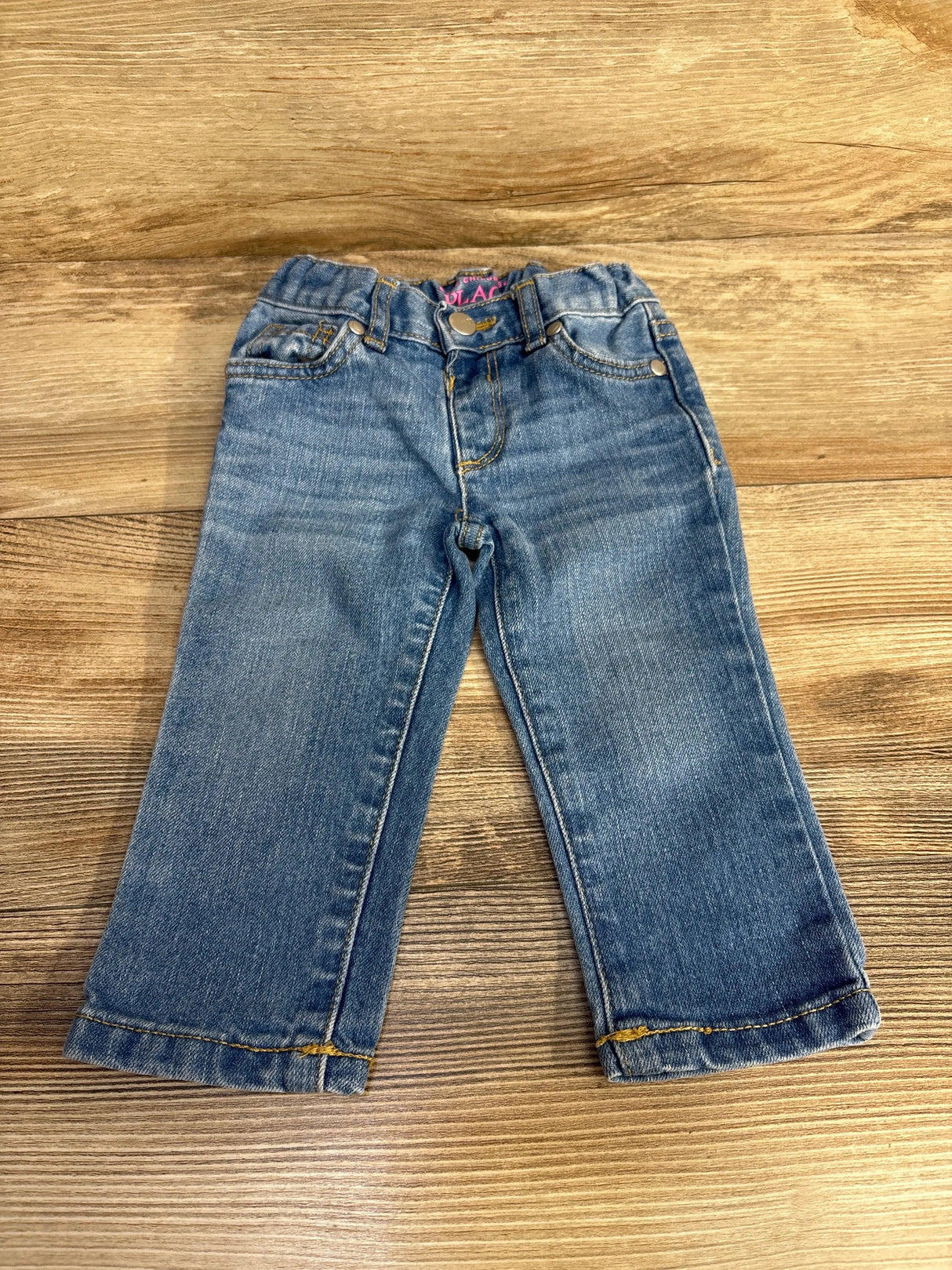 Front view of Children’s Place skinny blue toddler jeans showing elastic waist faded wash on wood background