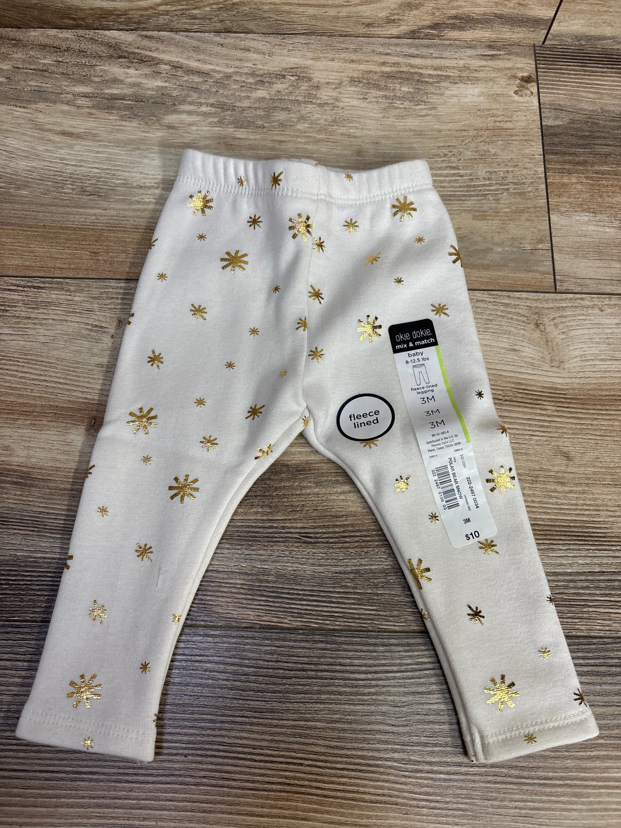 White fleece-lined baby leggings with gold star prints, size 3M, on wood floor