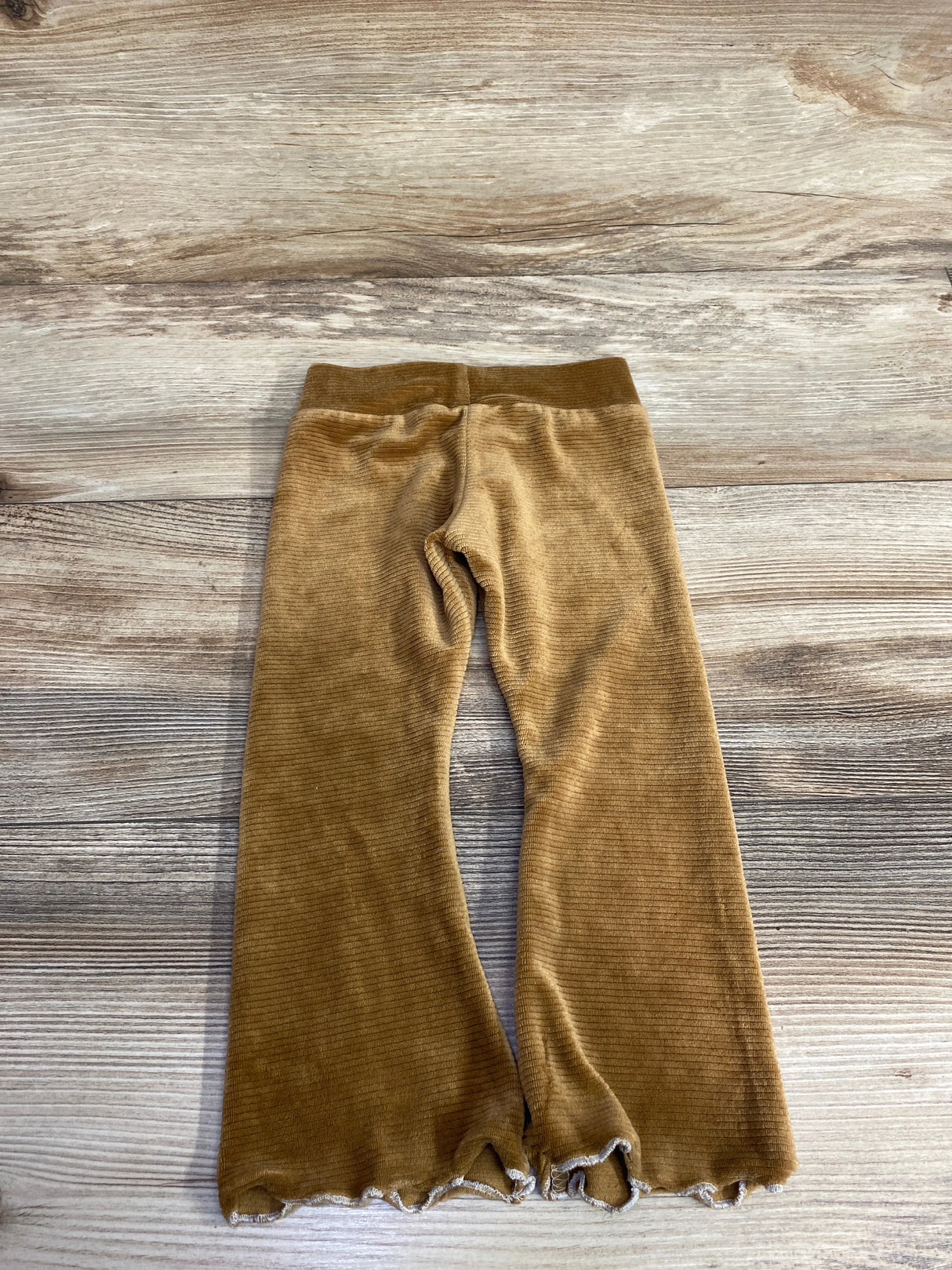 Brown ribbed baby pants with elastic waistband and frilled hems on wooden surface