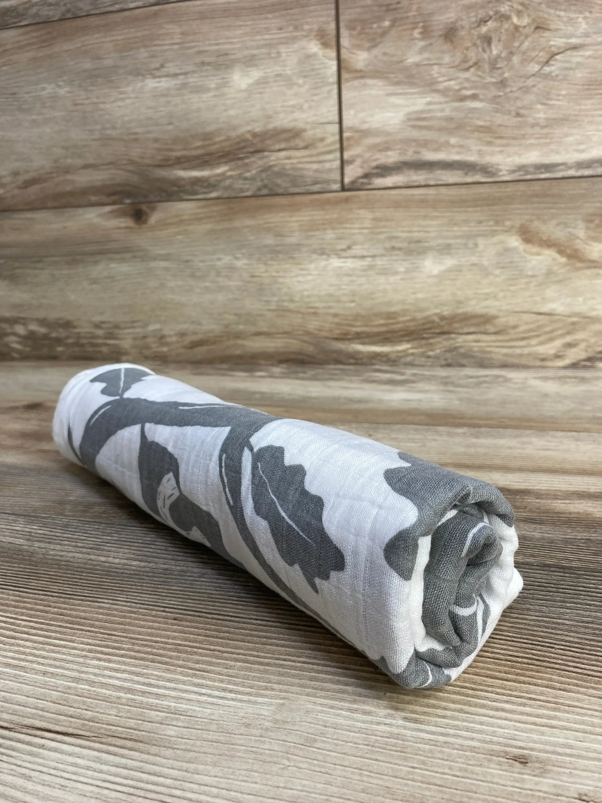 Angled view of Baby Wings Height Milestone Blanket, Tree showing gray tree and leaf print rolled on a wood floor