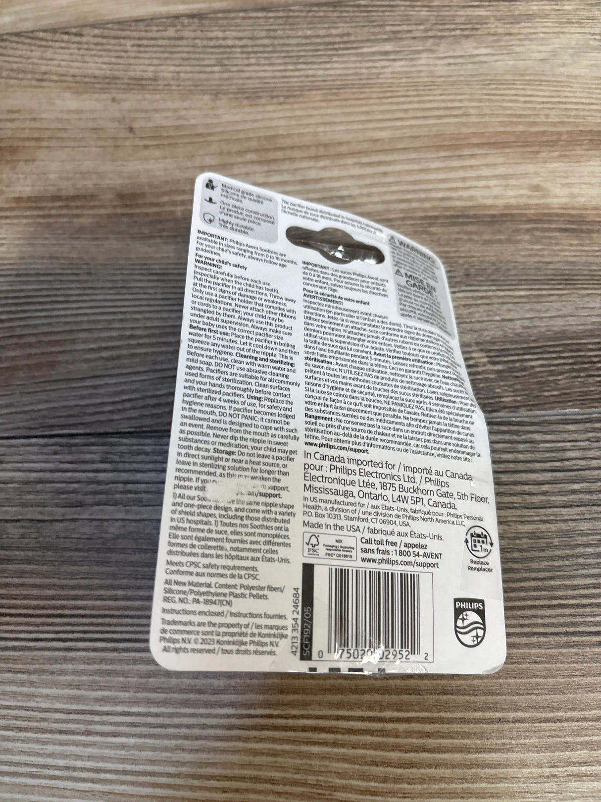 Back of Philips Avent Soothie pacifier packaging with safety instructions, barcode, and USA manufacturing details on wood surface.