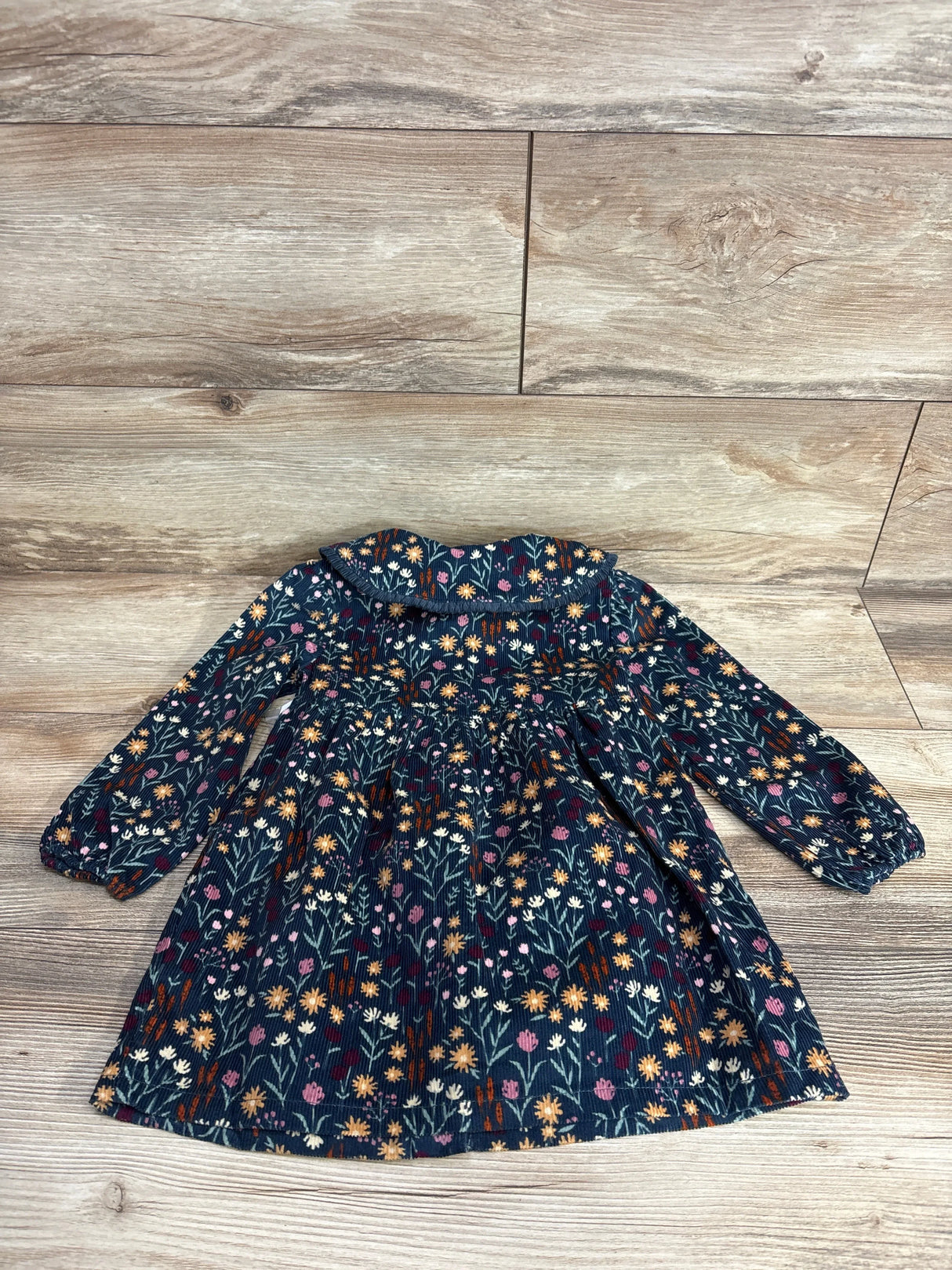 Long sleeve floral toddler dress with yellow and pink flowers on a dark background, laid on wood