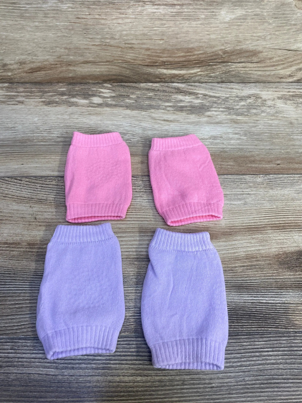 Top down view of baby crawling knee pads showing two pink and two lilac pairs with ribbed cuffs on wood background