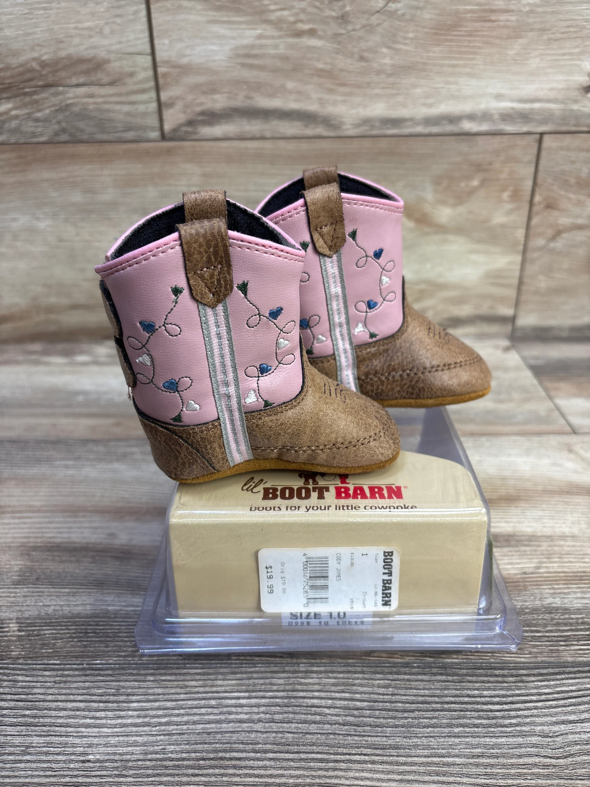 Three-quarter view of Old West Poppets girls pink cowboy boots showcasing floral embroidery and brown toe on a wooden tabletop