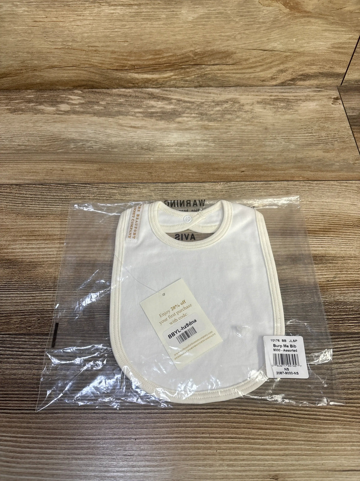 Front view of The Beaufort Bonnet Company Burp Me Bib showcasing its cream color and rounded trim in clear packaging