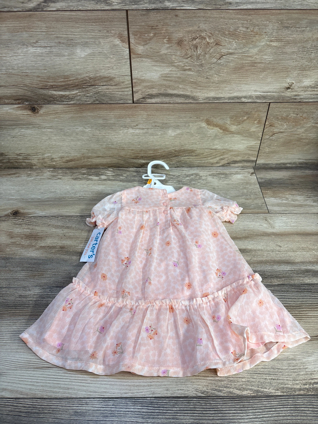 Front view of pink floral baby dress and matching bloomers on hanger showing ruffled hem and puff sleeves on wood background