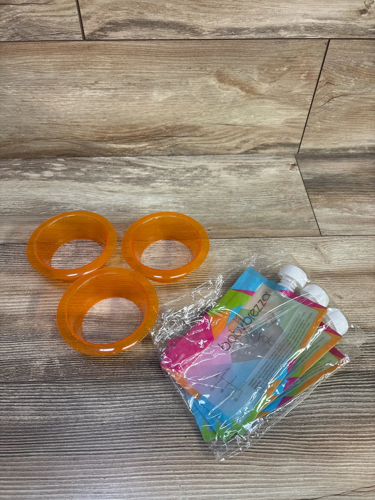 Close-up of Baby Brezza One Step Baby Food Maker Deluxe accessories showcasing three orange rings and packaged parts on a wood surface