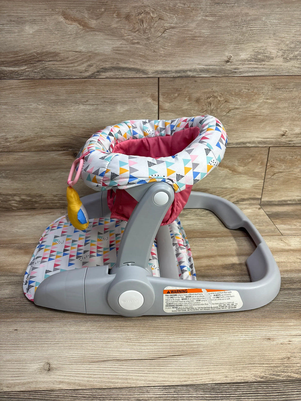Colorful baby walker with geometric triangle print and gray plastic frame on wood floor