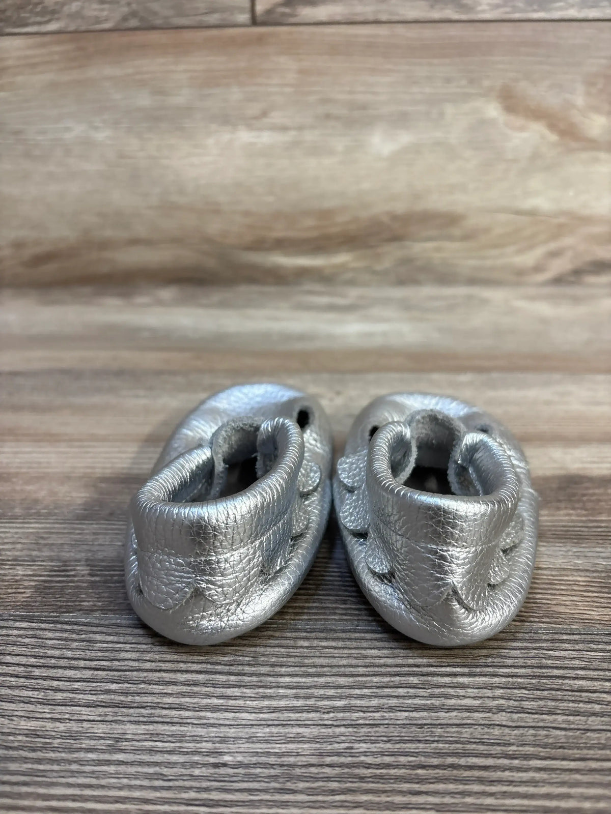 Silver leather baby moccasins on wood background, gently used infant shoes
