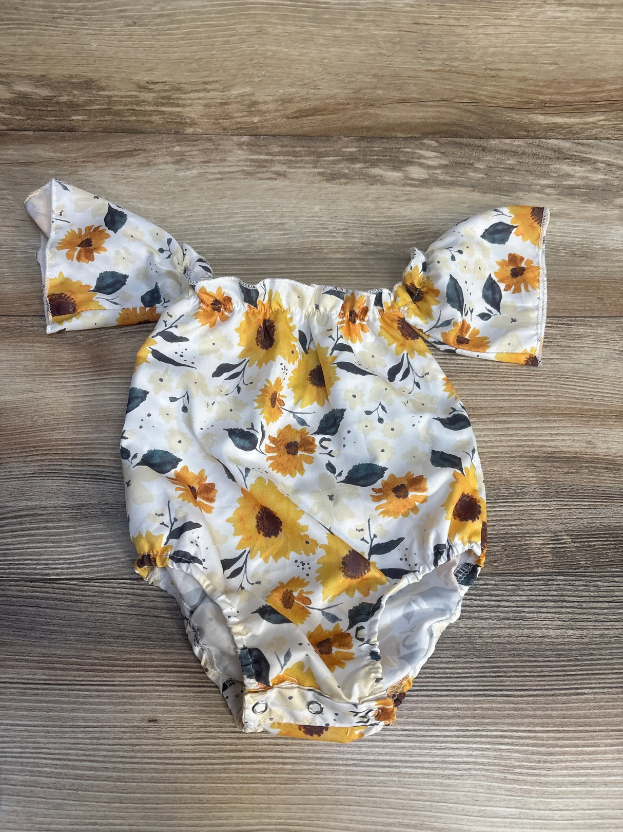 Floral baby romper with yellow sunflowers, flutter sleeves, snap bottom, on wood background.