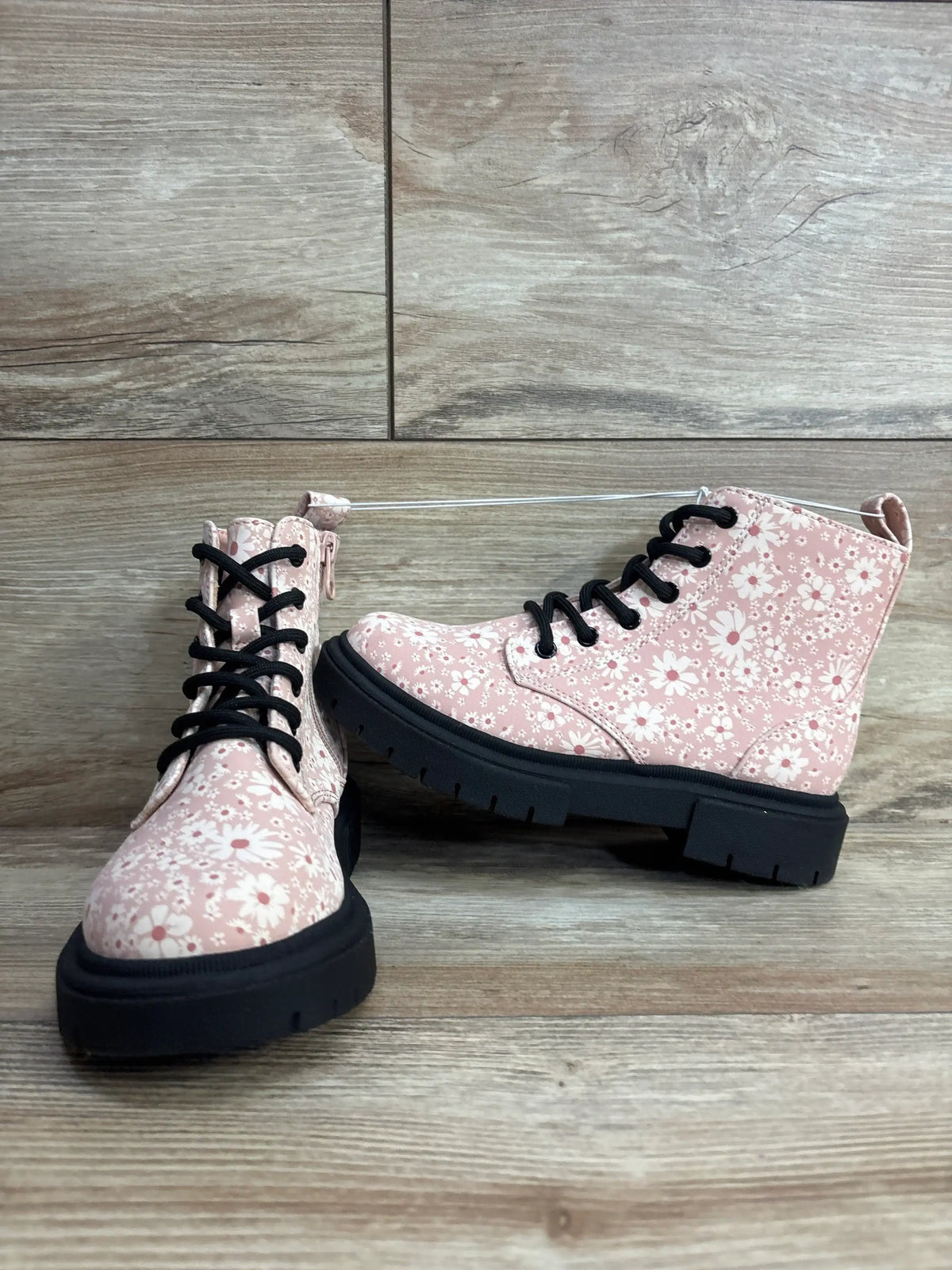 Pink floral kids boots with black laces and chunky soles on wood floor background