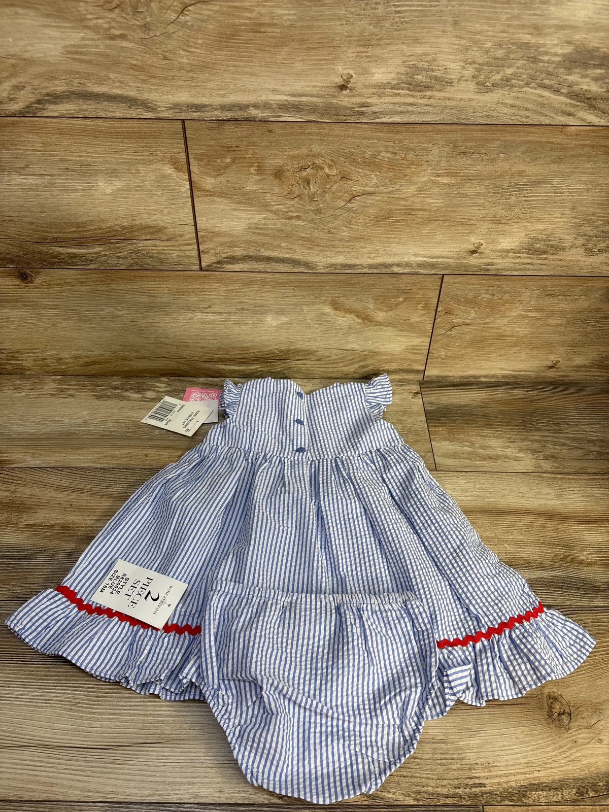 Top down view of Rare Editions blue seersucker dress and bloomers set showcasing striped fabric and red trim on wood floor