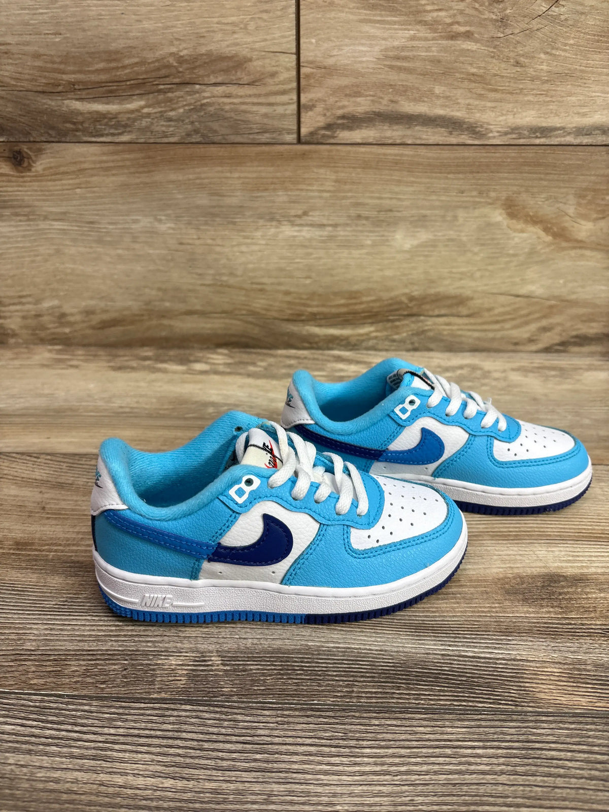 Front and side views of Nike Force 1 LV8 PS Split sneakers showcasing Light Photo Blue and white color blocking with perforated toe boxes on wood grain