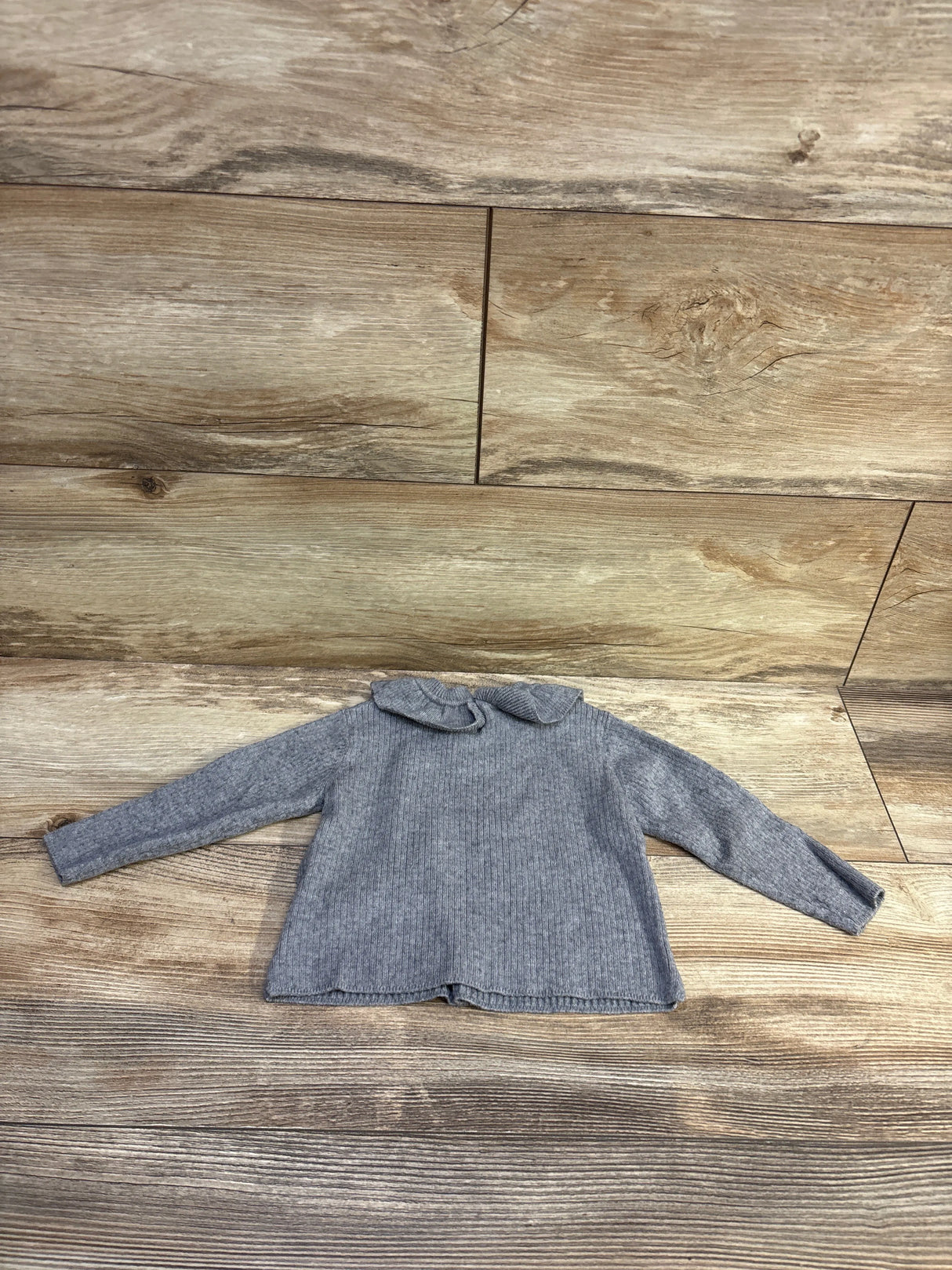 Front view of Zara grey ruffle collar sweater, size 6 to 9 months, with long sleeves and ribbed knit on wood