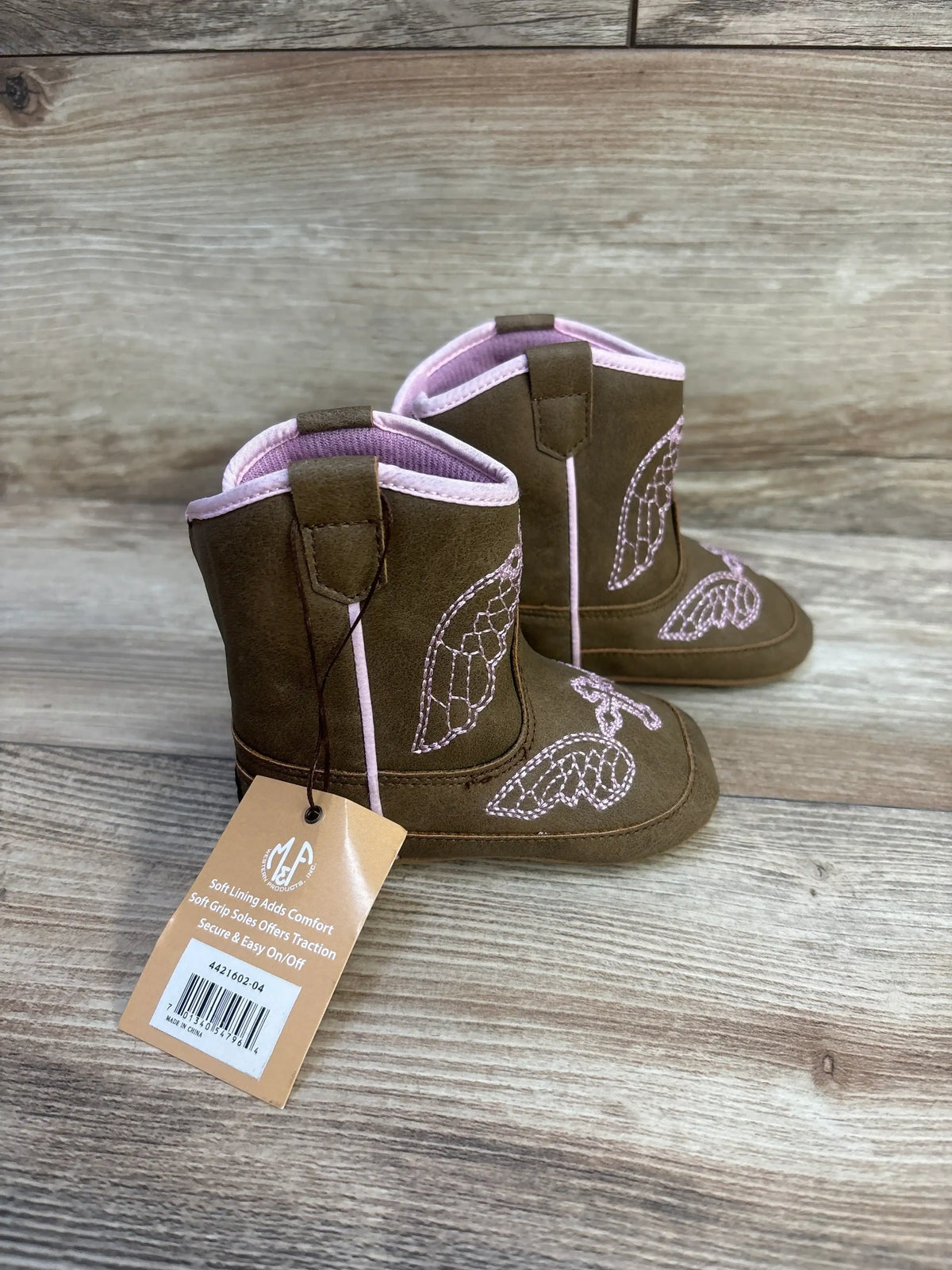 Three-quarter view of Twister Gracie Baby Buckers boots showcasing pink wing embroidery and pink trim on light wood background