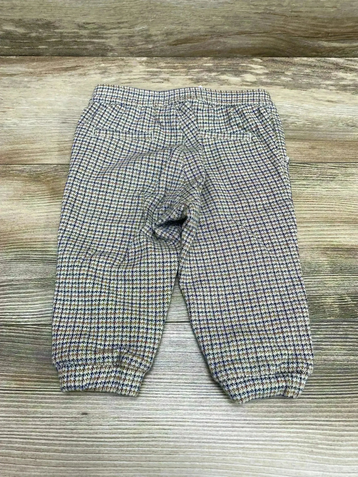 Top view of Janie and Jack brown houndstooth baby joggers with elastic waist and cuffed ankles on wood background