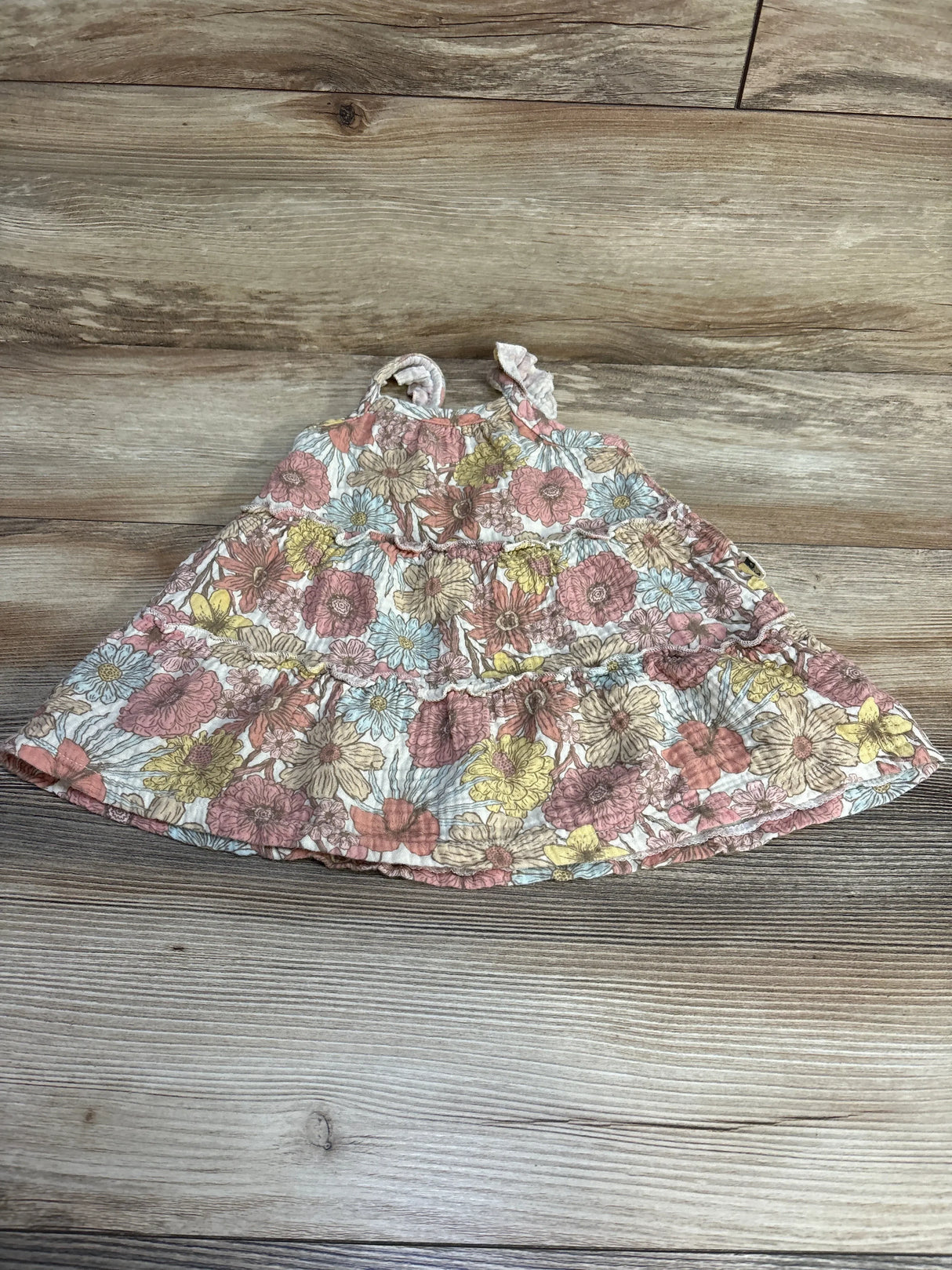 Front flat-lay of Rabbit + Bear floral baby dress (18 months) showcasing tiered ruffle skirt and shoulder tie straps on wood background