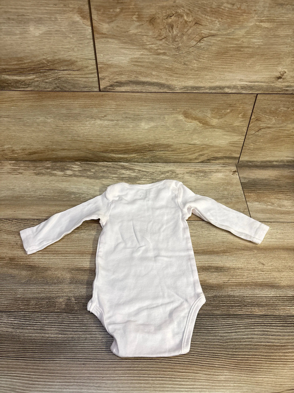 Back view of Rae Dunn pumpkin love bodysuit in pink, size 6 to 9 months, showing long sleeves on wood flooring