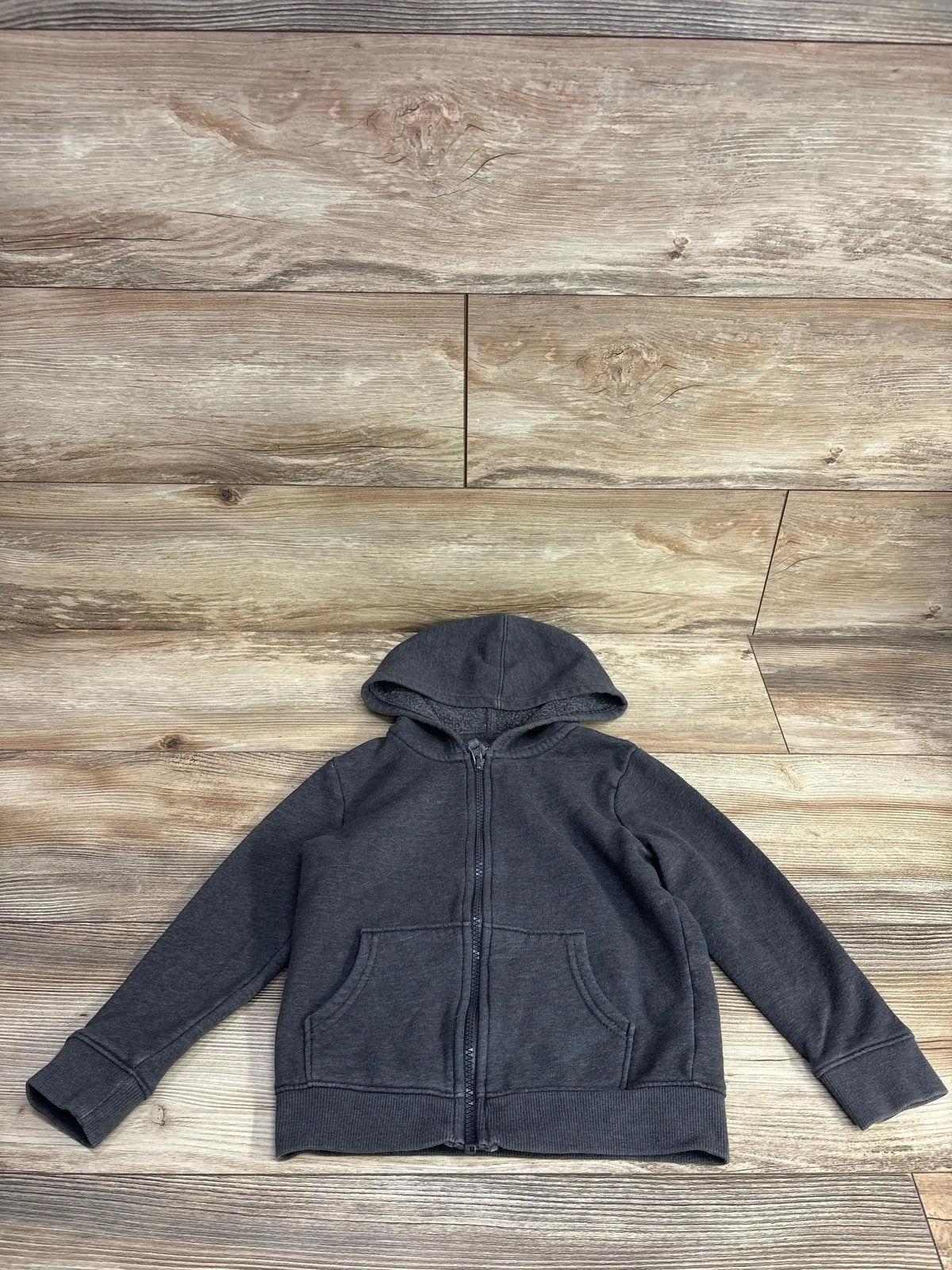 Dark gray children's zip-up hoodie with front pockets on wooden floor background