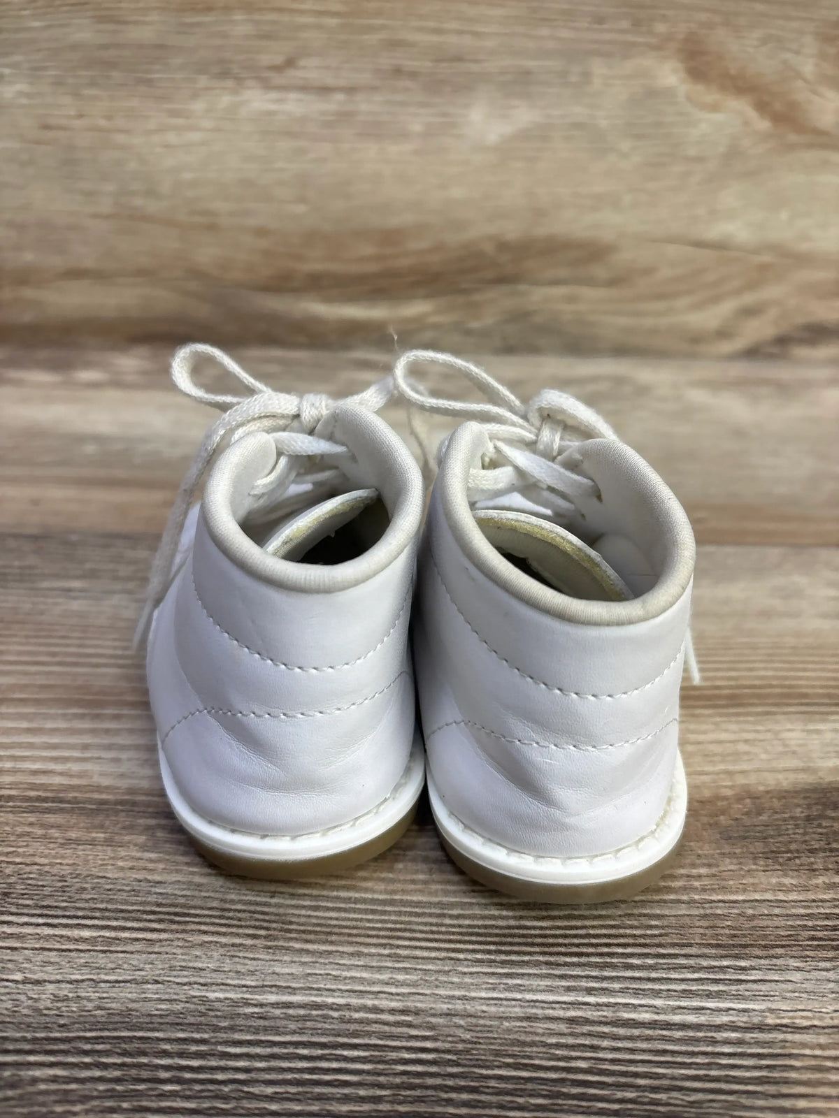 Rear view of white Teeny Toes first walker shoes showing padded ankle collars and lace-up ties on woodgrain background