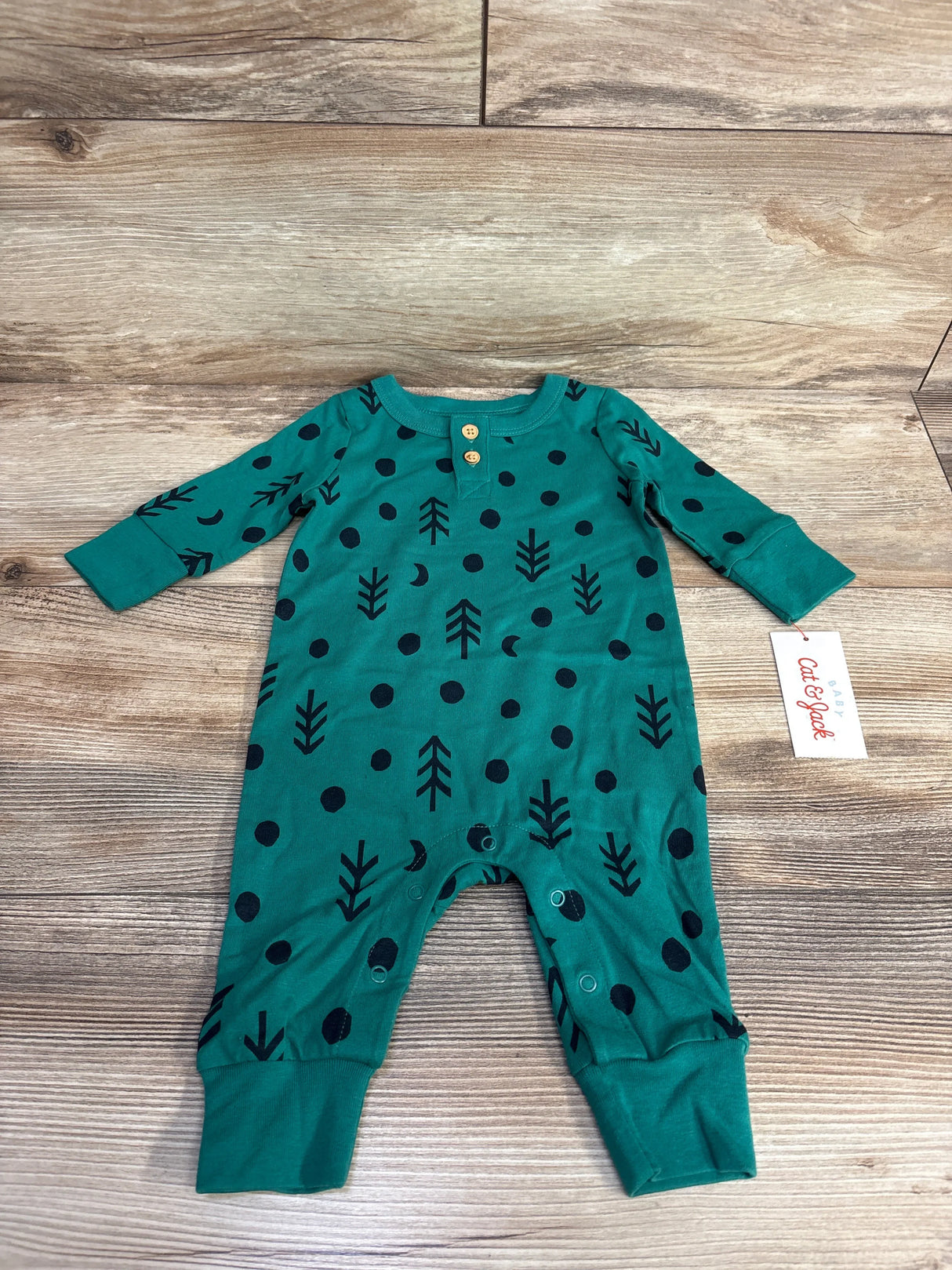 Green baby romper with black tree and dot pattern, long sleeves, wooden buttons, laid on wood floor