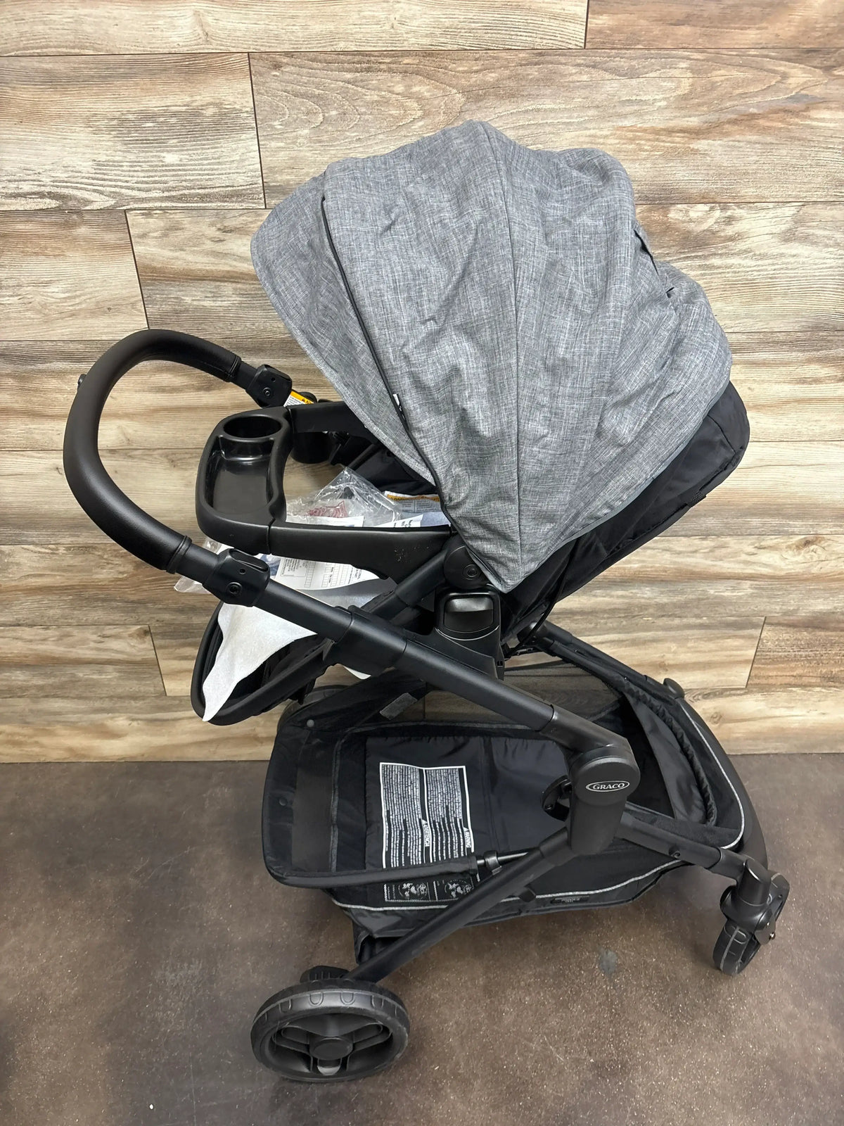 Gray Graco baby stroller with canopy, cup holder, and storage basket on wood floor