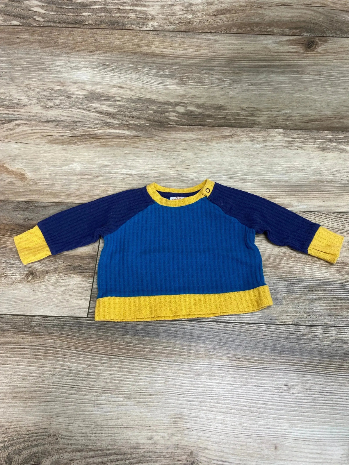 Flat lay of Cat & Jack Waffle Knit Shirt sz 0-3m in blue with navy raglan sleeves and yellow trim on wood plank floor