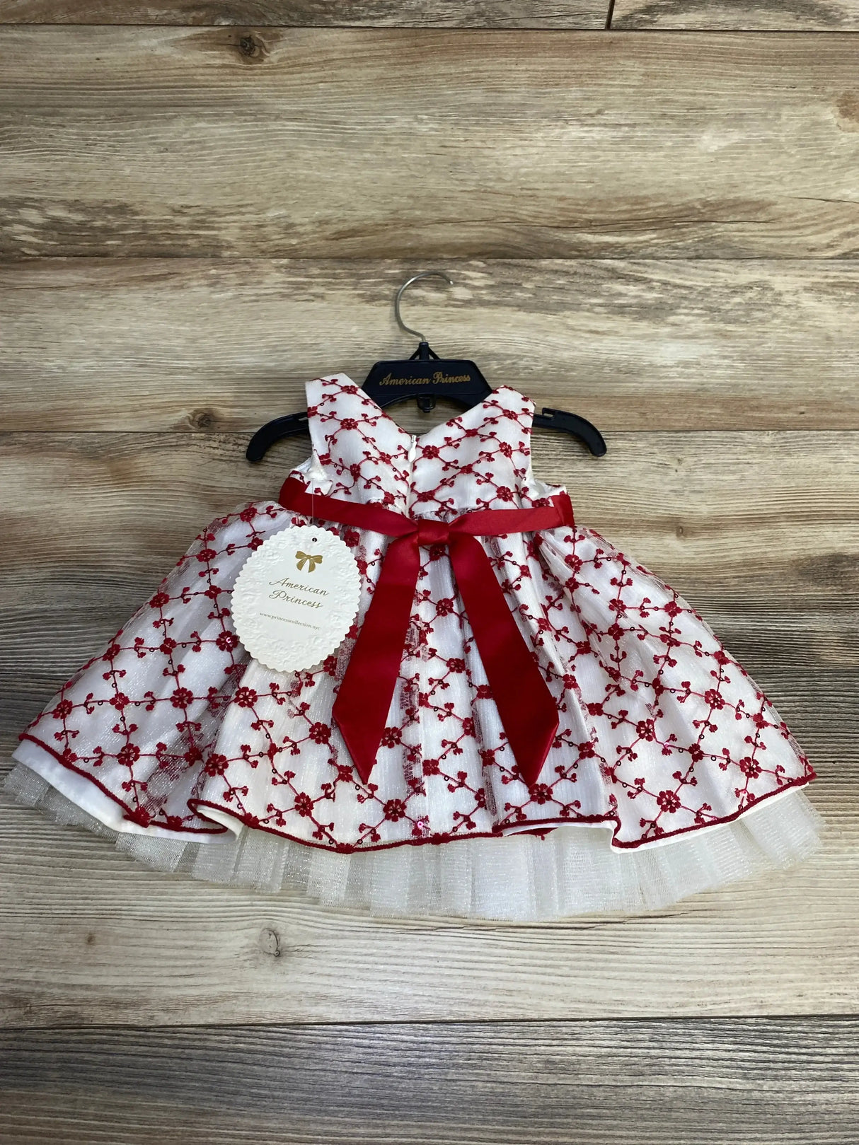Front view of white tulle baby dress (size 6 months) showcasing red floral embroidery and a red ribbon bow with matching bloomers on wood background