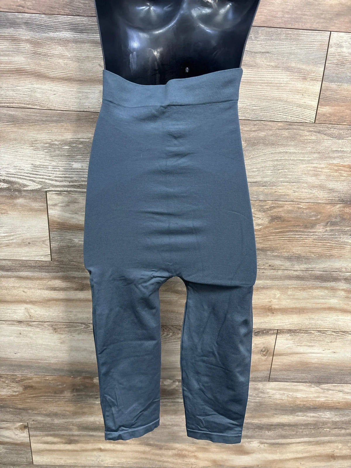 High-waisted grey shapewear leggings on black mannequin, wood background